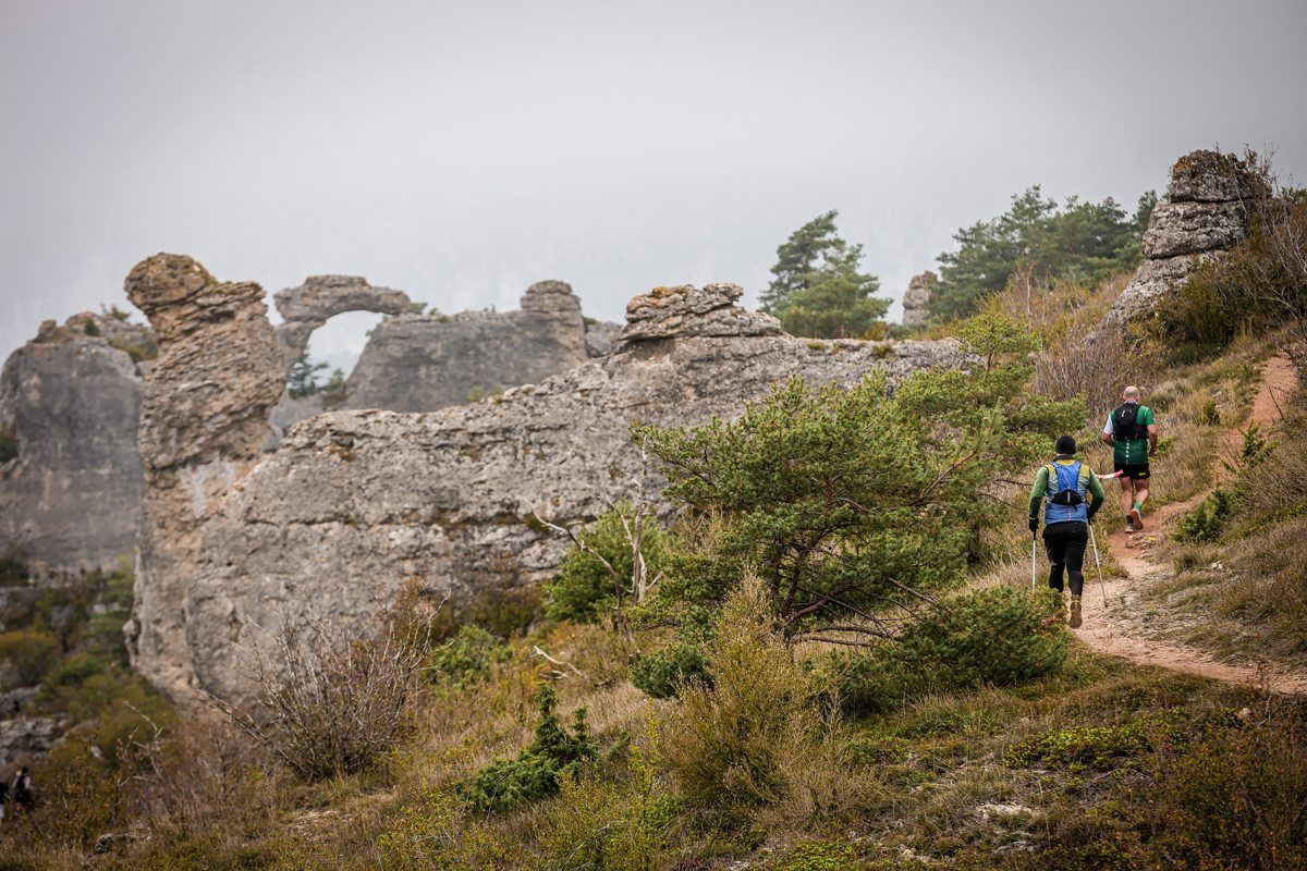 Deux coureurs sur un sentier au pied d'un chaos rocheux percé d'arches