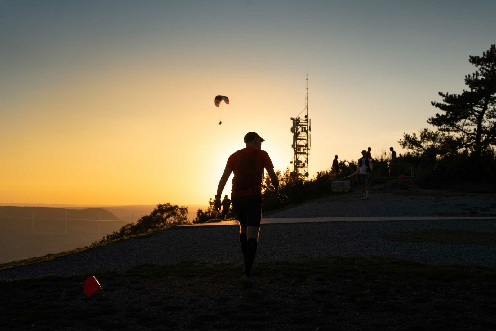 Silhouette d'un coureur sur le plateau au coucher du soleil, parapente dans le ciel