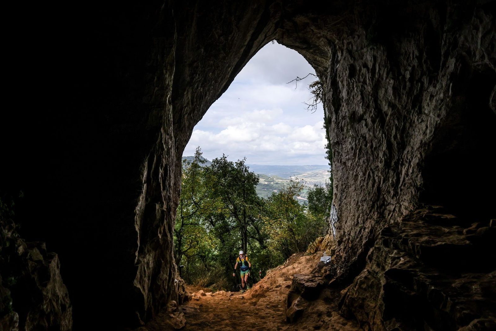 Un coureur passe sous une immense arche rocheuse, silhouette à contre-jour